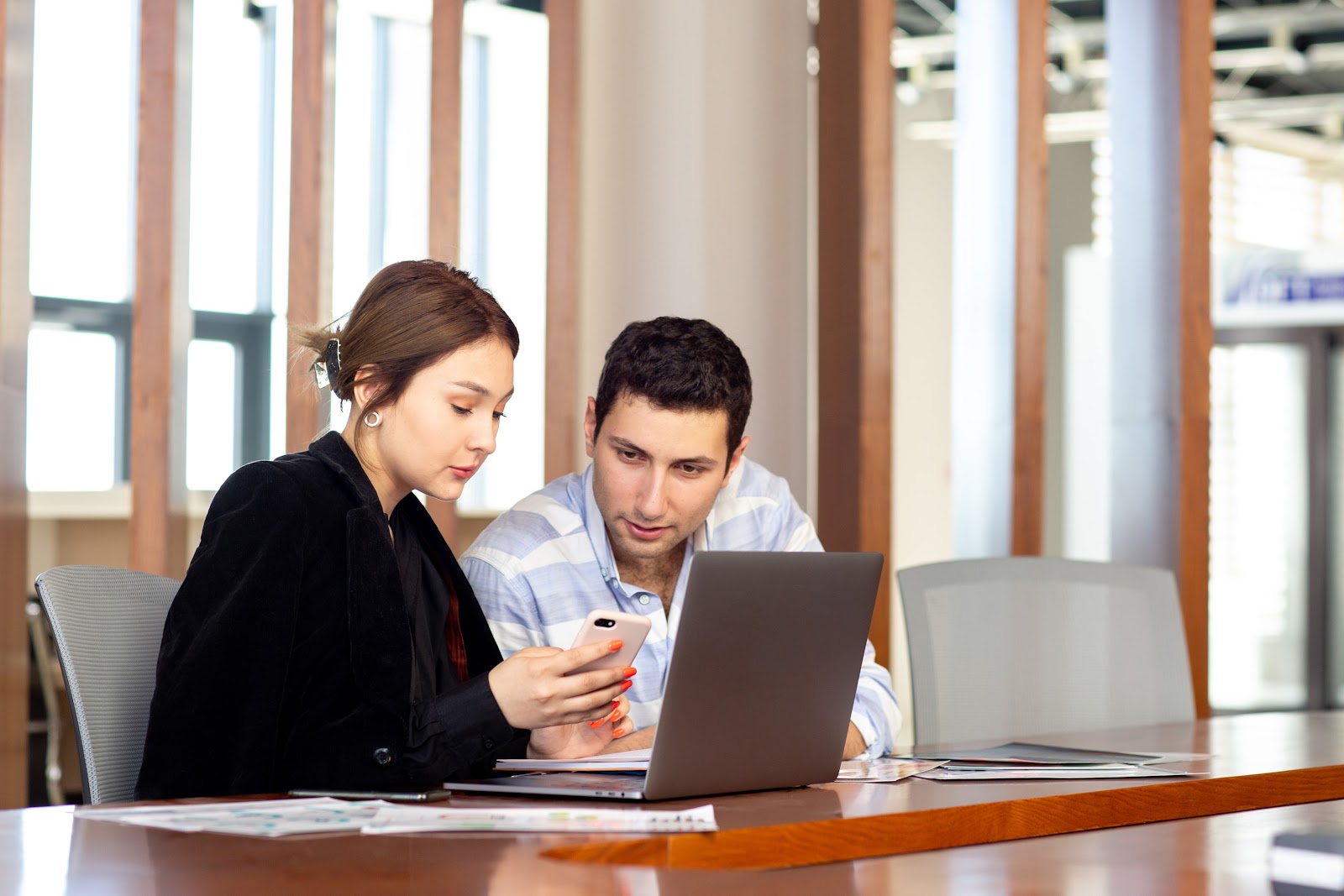 Man and woman looking at phone with a laptop on the table